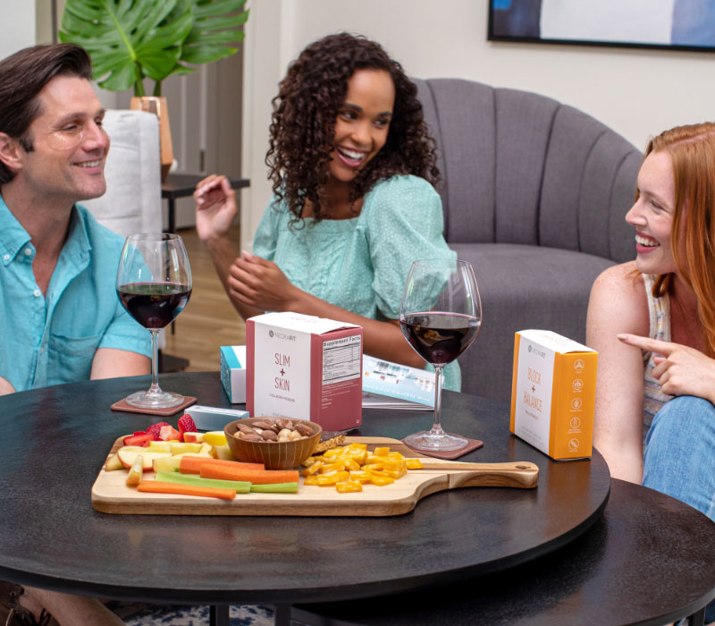 Friends sitting around a coffee table enjoying food and wine while talking about becoming a Neora Brand Partner and sampling NeoraFit and Eye Patches.